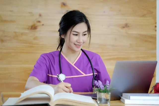 a nurse is looking at a laptop while writing